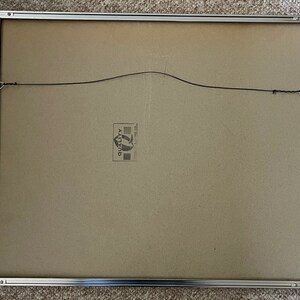 May include: The back of a silver picture frame with a brown cardboard backing. A small white label with the word "Quality" is visible on the backing.