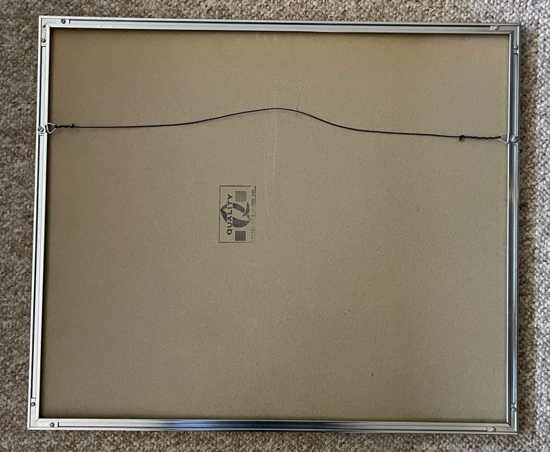 May include: The back of a silver picture frame with a brown cardboard backing. A small white label with the word "Quality" is visible on the backing.