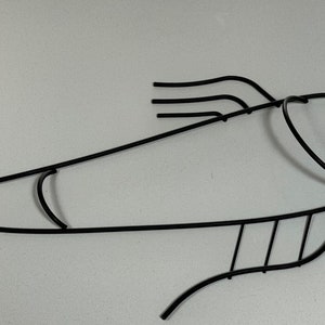 May include: Black metal fish wall decor with a stylized design. The fish has a curved body and a rounded head with a simple eye.