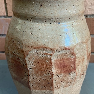 May include: A beige ceramic jar with a lid and a brown and beige geometric pattern. The jar has a rough, textured surface.
