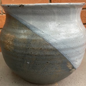 May include: A large, round, gray ceramic planter with a white glaze on one half. The planter has a rough, textured surface.