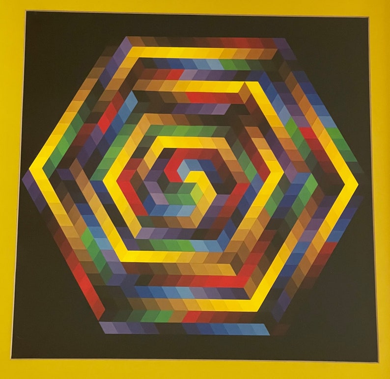 May include: A framed abstract geometric art print. The artwork features a colorful, multi-layered hexagonal design with a spiral center. The color palette includes yellow, red, blue, green, and brown hues against a black background.