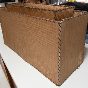 May include: Three rectangular brown woven storage boxes of varying sizes. The boxes have a textured pattern and are stitched together with dark thread. The boxes are empty and sit on a white surface.