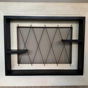 May include: A white wood frame with a black inner frame and a black lattice design. The frame has two shelves.
