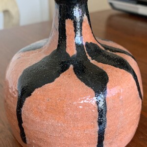 May include: A small, round, terracotta vase with black glaze dripping down the sides. The vase has a narrow neck and a wide base.