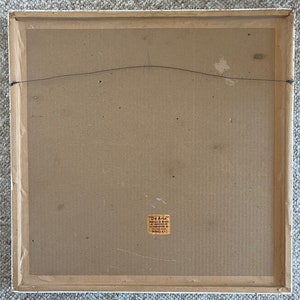 May include: Back of a framed artwork with a white wooden frame. The artwork backing is cardboard with a wire for hanging. A small sticker in the lower right corner reads "De Arte".