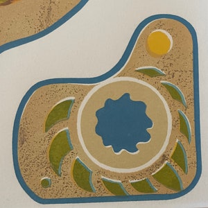 May include: A tan and brown ceramic tile with a blue and green design. The tile has a circular design with a blue center and green leaves around it. There is a yellow circle in the upper right corner of the tile.