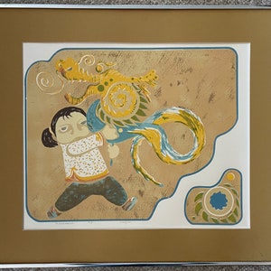 May include: A framed print of a colorful illustration depicting a young person holding a blue and yellow dragon with a swirling tail. The background is a textured tan color.