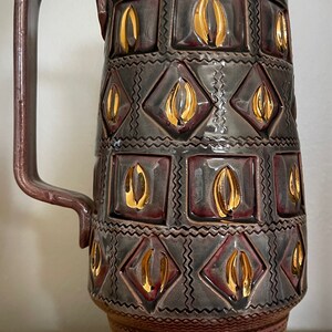 May include: A large, purple ceramic pitcher with a gold rim and geometric pattern. The pitcher has a wide base and a handle.