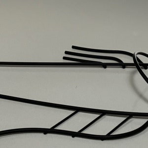 May include: Black metal fish sculpture with a stylized design. The fish is depicted in a swimming position with its tail curved upwards and its fins spread out.