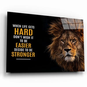 Könnte beinhalten: Motivierender Wandkunstdruck mit einem Löwengesicht und dem Text "When life gets hard, don't wish it to be easier, decide to be stronger" in Gelb und Weiß auf schwarzem Hintergrund.