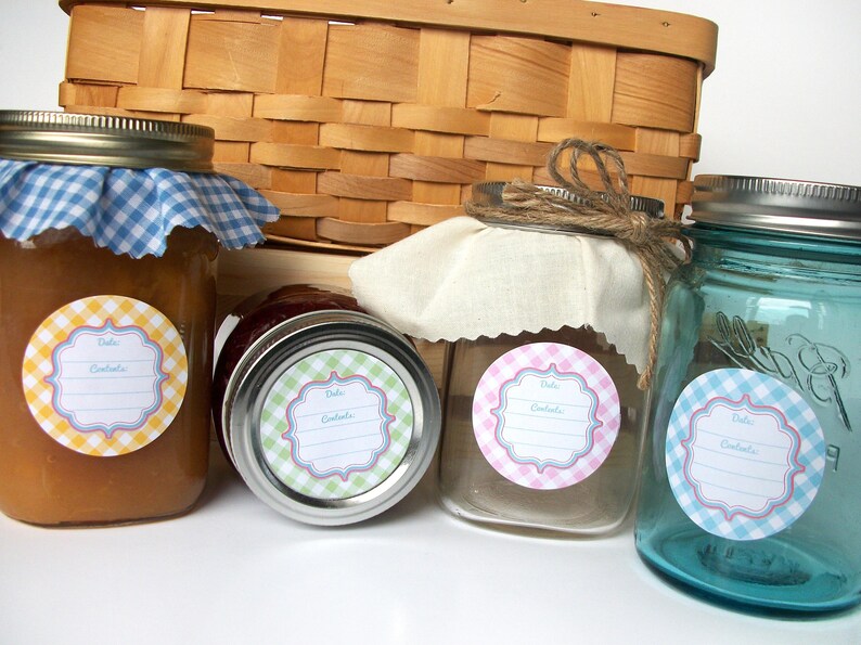 May include: Four glass jars with labels featuring a gingham pattern and the text "Date & Contents". The jars are filled with different coloured liquids and are arranged in a row on a wooden surface.
