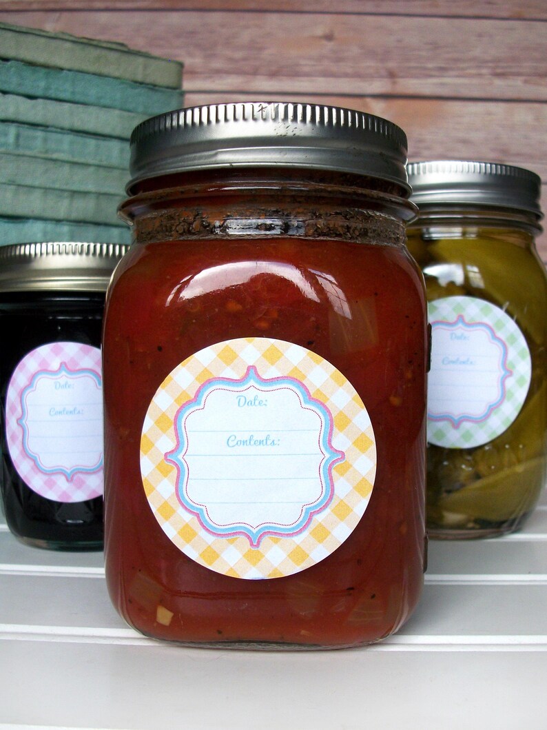 May include: Three glass jars with silver lids and labels. The labels are round and have a yellow and white checked pattern with a blue and pink border. The labels have the words "Date:" and "Contents:" printed on them. The jars are filled with different coloured liquids.