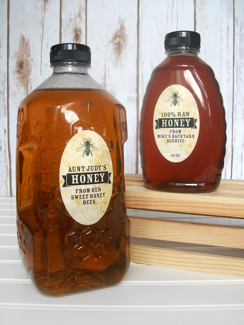 Vintage looking oval honey labels on the front of honey bottles filled with honey. Label art has a realistic honey bee up top with printed text for 100% Raw honey.