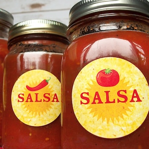 May include: Three glass jars filled with red salsa, each with a round yellow label that says "SALSA" in red letters. The labels have a sunburst design and a red tomato or chili pepper.
