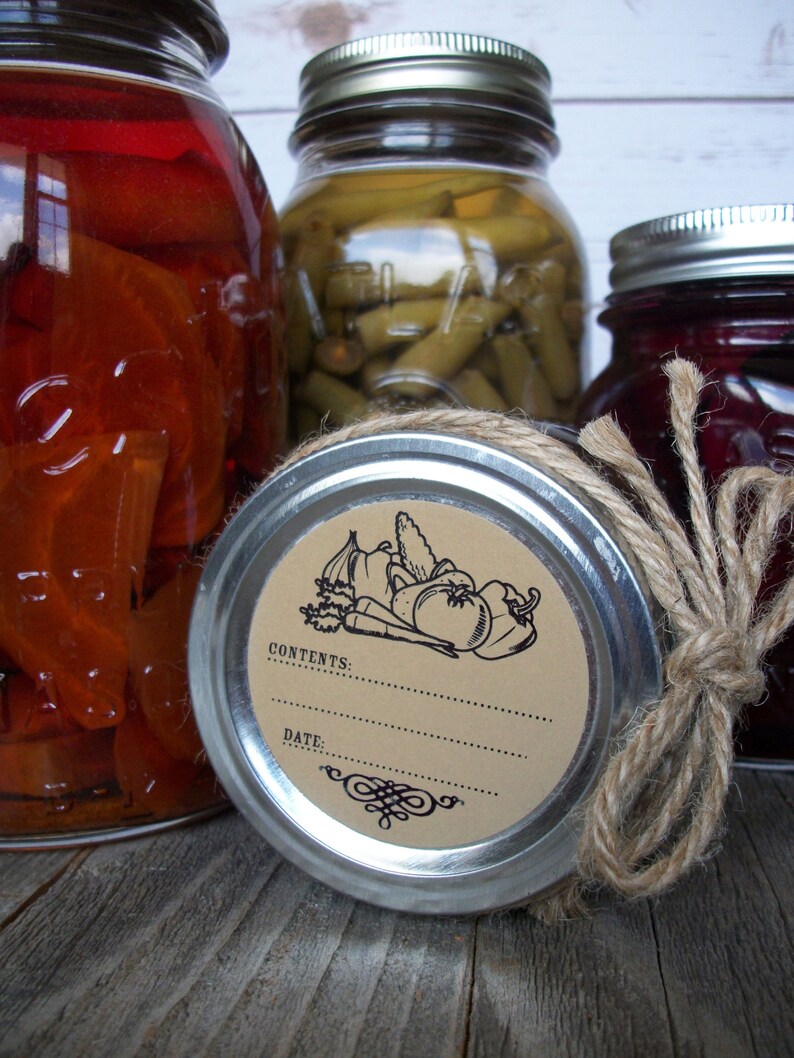 May include: Three glass jars with lids, two with brown twine tied around the lids. The jar in the center has a brown paper label with a black illustration of vegetables and the text "CONTENTS: DATE:".