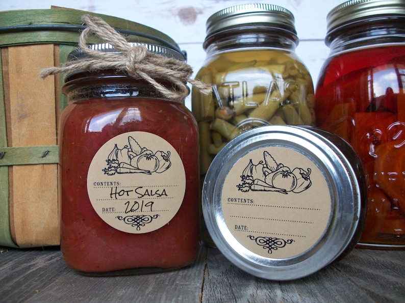 May include: Three glass jars with brown paper labels. The jar on the left contains red salsa with a label that reads "Hot Salsa 2019". The jar in the middle contains green beans and the jar on the right contains red peppers.