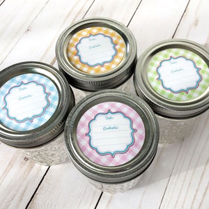 May include: Four glass jars with silver lids and colourful gingham patterned labels. The labels have a space for "Date:" and "Contents:" and a decorative border. The jars are on a light wood surface.
