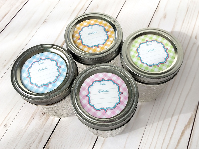 May include: Four glass jars with silver lids and colourful gingham patterned labels. The labels have a space for "Date:" and "Contents:" and a decorative border. The jars are on a light wood surface.