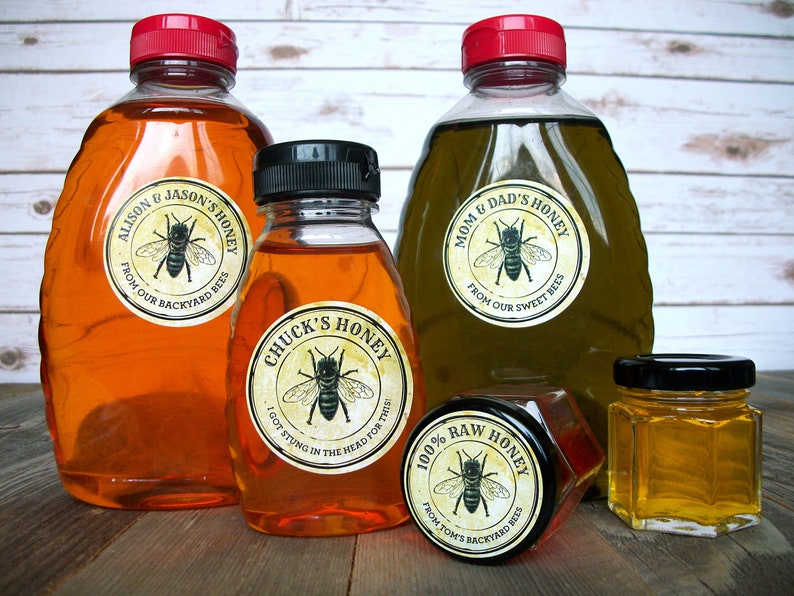 May include: Four glass jars of honey with labels featuring bee illustrations and text. The labels read "Alison & Jason's Honey", "Chuck's Honey", "Mom & Dad's Honey", and "100% Raw Honey".