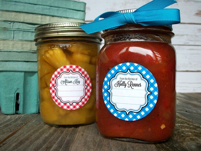 May include: Two glass jars with red and blue gingham patterned labels. The labels have a white background with black text that reads "From the Kitchen of Alison Kay" and "From the Kitchen of Holly Renner".