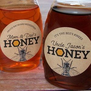 May include: Two glass honey jars with brown paper labels. The labels have a bee illustration and text that reads "Mom & Dad's Honey" and "Uncle Jason's Honey".