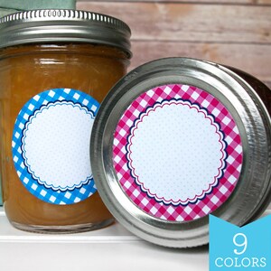 May include: Two glass jars with metal lids. The jars are filled with a light brown substance. Each jar has a round label with a white background and a scalloped border. The label on the left jar has a blue and white gingham pattern. The label on the right jar has a pink and white gingham pattern. The text "9 COLORS" is printed in blue on a light blue background.