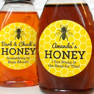 May include: Two glass honey jars with yellow and black bee-themed labels. The labels have honeycomb patterns and say "Barb & Chuck's Honey Something to Buzz About!" and "Amanda's Honey I Got Stung in the Head for This!"