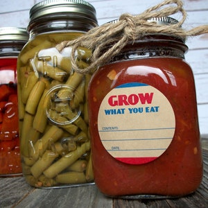 May include: Three glass jars with lids, filled with preserved food. The jar on the right has a brown label with the text "GROW WHAT YOU EAT" and a blank space for "CONTENTS" and "DATE".