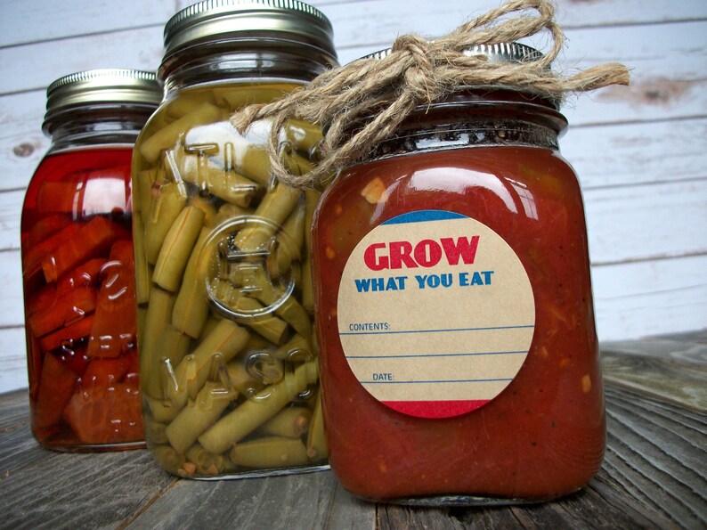 May include: Three glass jars with lids, filled with preserved food. The jar on the right has a brown label with the text "GROW WHAT YOU EAT" and a blank space for "CONTENTS" and "DATE".
