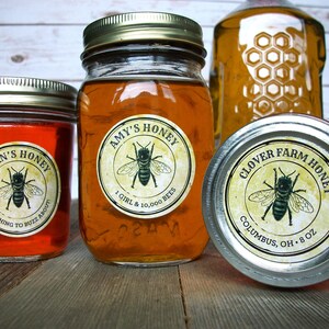 May include: Three glass jars of honey with labels. The labels are round and have a vintage design with a bee illustration. The labels read "Alan's Honey", "Amy's Honey", and "Clover Farm Honey".