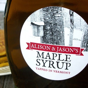 May include: A white round label with black text and a red ribbon reads "Alison & Jason's Maple Syrup Tapped in Vermont". The label is on a brown glass bottle.