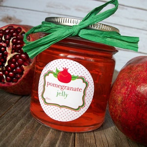 May include: A jar of red pomegranate jelly with a white label that says "pomegranate jelly" and has a red pomegranate illustration. The jar is tied with a green ribbon and there are two whole pomegranates next to it.