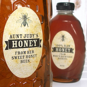 Vintage looking oval honey labels on the front of honey bottles filled with honey. Label art has a realistic honey bee up top with printed text for honey.