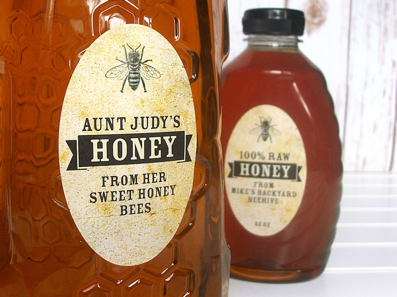 Vintage looking oval honey labels on the front of honey bottles filled with honey. Label art has a realistic honey bee up top with printed text for honey.