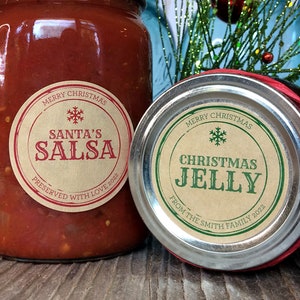 Puede incluir: Un frasco de vidrio con salsa roja y una etiqueta redonda color canela que dice MERRY CHRISTMAS SANTA'S SALSA PRESERVED WITH LOVE 2022 y un frasco de mermelada con la etiqueta MERRY CHRISTMAS CHRISTMAS JELLY FROM THE SMITH FAMILY 2022.