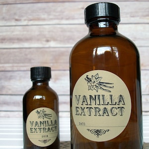 May include: Two brown glass bottles with black lids and round labels. The labels are cream colored with black text that reads "Vanilla Extract". The smaller bottle has a date of "2018" on the label.