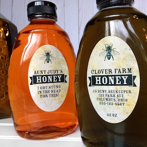 Vintage looking oval honey labels on the front of honey bottles filled with honey. Label art has a realistic honey bee up top with printed text for honey.