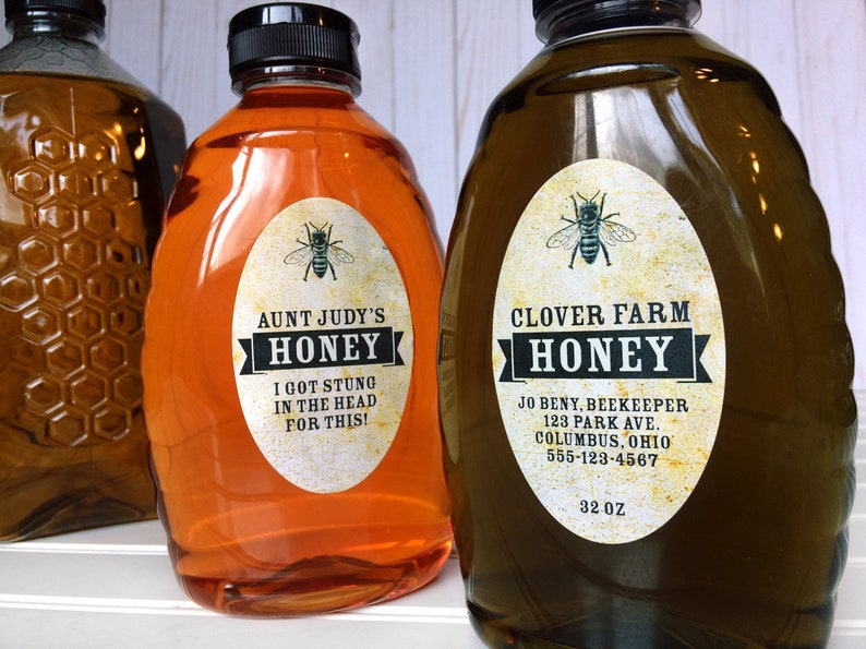Vintage looking oval honey labels on the front of honey bottles filled with honey. Label art has a realistic honey bee up top with printed text for honey.