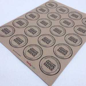 May include: A sheet of twenty circular brown kraft paper labels featuring black text that reads Apple Pie Moon Shine, XXX Home Brewed, Just For Your Kick, and Drink Responsibly. The CanningCrafts logo is printed in red at the bottom left.