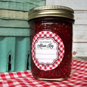 May include: A glass jar filled with red jam with a red and white gingham patterned label that says "From the Kitchen of Alison Kay".