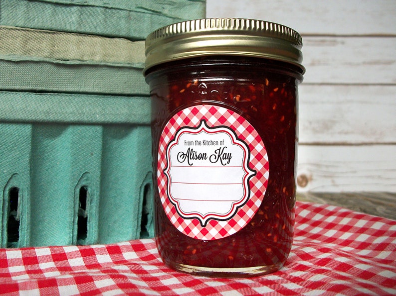 May include: A glass jar filled with red jam with a red and white gingham patterned label that says "From the Kitchen of Alison Kay".