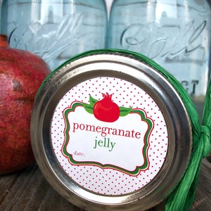May include: A silver jar lid with a white and red polka dot label that says "pomegranate jelly" with a green border and a red pomegranate illustration. The label also has the words "date:" printed on it.