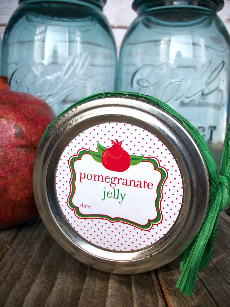 May include: A silver jar lid with a white and red polka dot label that says "pomegranate jelly" with a green border and a red pomegranate illustration. The label also has the words "date:" printed on it.