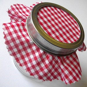 May include: A glass jar with a red and white gingham fabric lid. The lid is ruffled and has a silver metal band.