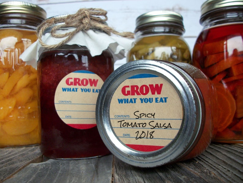 May include: Four glass jars with metal lids and labels. The labels are brown with white text and a red and blue border. The text on the labels reads "Grow What You Eat". One jar has a label that says "Spicy Tomato Salsa" and "2018".