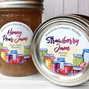 May include: Two glass jars of homemade jam with colorful labels. The jar on the left is honey pear jam with a white label featuring a watercolor illustration of jars and the text "Return Jar to Keep Me Jammin' Honey Pear Jam From Jan's Kitchen". The jar on the right is strawberry jam with a white label featuring a watercolor illustration of jars and the text "Homemade in Nancy's Kitchen Strawberry Jam Spring 2022".