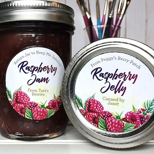 May include: Two glass jars with silver lids, one filled with raspberry jam and the other with raspberry jelly. Both jars have round labels with watercolor illustrations of raspberries and text that reads "Raspberry Jam" and "Raspberry Jelly".