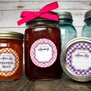 May include: Three glass jars with lids, two with labels that say "From the Kitchen of Alison Kay" and one with a label that says "From the Kitchen of Amanda Jo". The labels are round and have a gingham pattern. The jars are filled with different colored preserves.