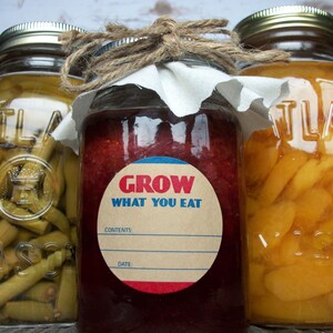 May include: Three glass jars with lids, filled with preserved foods. The center jar has a red and blue circular label that reads "Grow What You Eat".